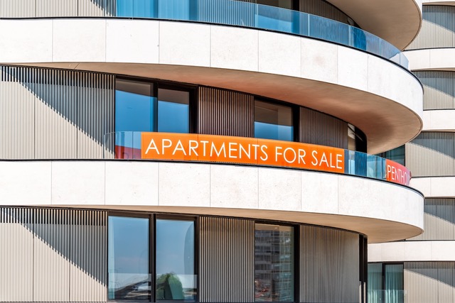 An apartment building with an orange for sale sign on the balcony is part of the property sales process for this multi-family building.